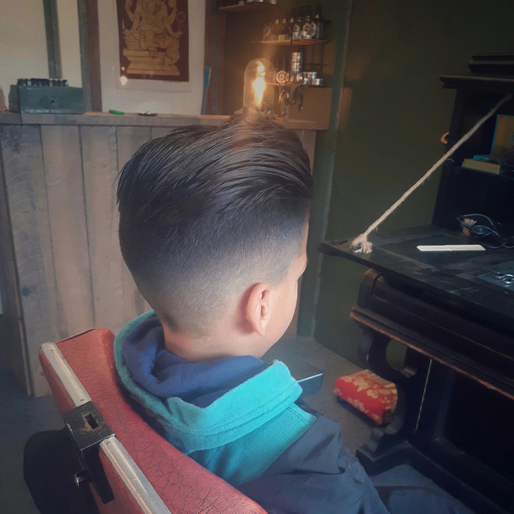 Jongen in de kappersstoel met een strak opgeschoren overloop en volume bovenop